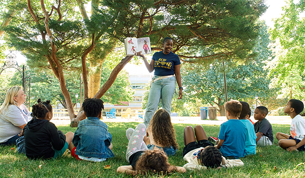 Image of a camp leader reading a story to students outside.
